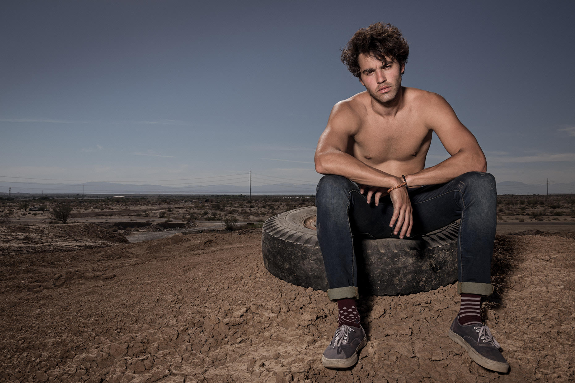 Environmental portrait of a man sitting on a tire in the California desert by photographer Jason Tracy